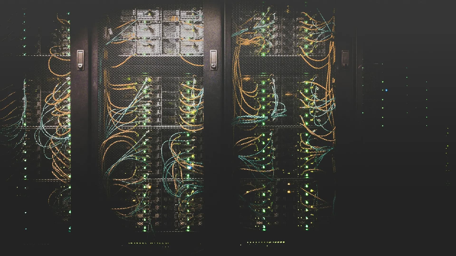 Des baies de serveurs dans l'obscurité, parcourues de câbles ambre et cyan et de diodes vertes
